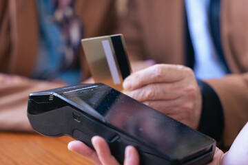 Unrecognizable senior couple at an outdoor cafe making a card payment. Both wearing trendy outfits and sunglasses. Ideal for retirement, finance, lifestyle, and senior couple relationship concepts. 