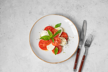 Caprese salad with sliced tomatoes, mozzarella and basil on a plate on a white background