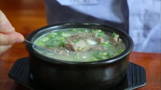 Person stirring a bowl of ox bone soup with spoon