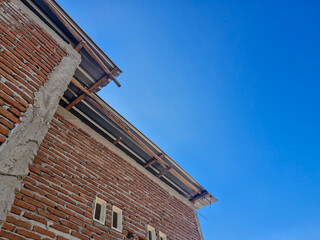 Negative space of a bright, clear sky with a semi-completed house in the corner, made of rough brick walls, plaster, and an asbestos roof