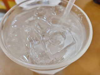 Close-up view of a plastic cup filled with clear ice cubes and water. A white straw is inserted into the drink.