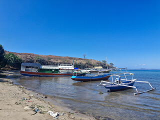 Traditional fishing boats docked in shallow coastal waters, surrounded by mangrove trees under a bright blue sky.