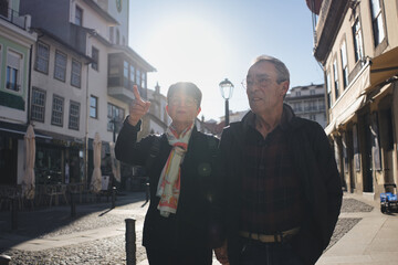 Happy senior tourist couple walking in city center during vacation, woman pointing at something interesting while exploring a new city together