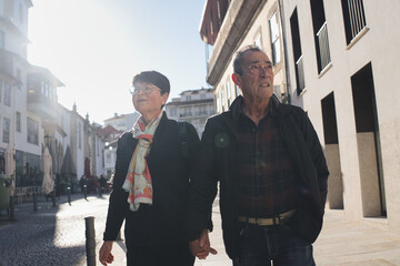 Happy retired tourists enjoying a sunny day, walking hand in hand down a charming european city street, discovering new sights and creating joyful memories together
