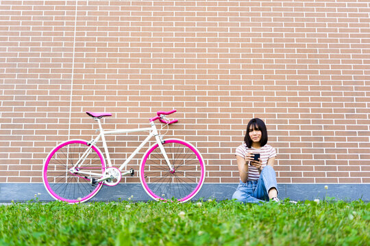 Young woman with mobile phone sitting by bicycle on footpath