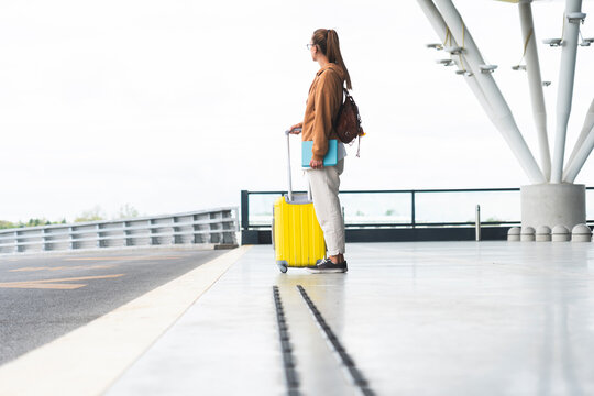 Young woman with wheeled luggage standing at airport