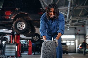 Brand new tire. Male mechanic is with car in garage