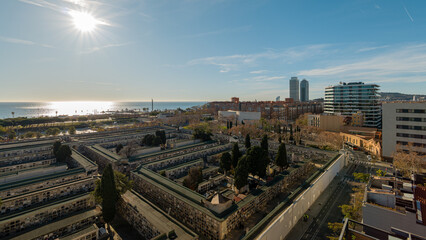 Fototapeta premium Wide view of seaside historic cemetery and Barcelona skyline in distance under clear sky