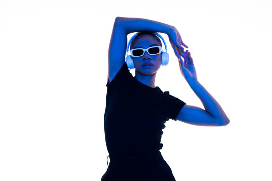 Fashionable woman posing with headphones and sunglasses in a studio with blue lighting