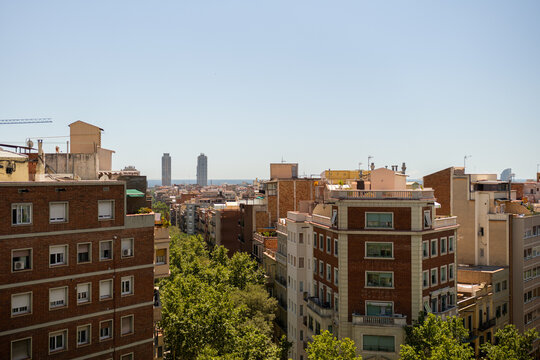 Cityscape with rows of residential buildings leading towards the distant sea under clear sky in Barcelona