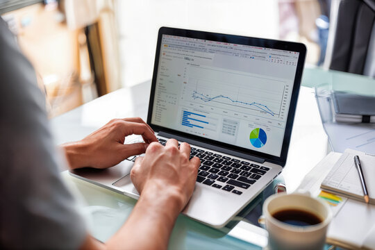 Business professional hands typing on laptop with analytics dashboard displayed on screen. Data visualization with line graphs, charts, statistics, and metrics. Office workspace with coffee cup - Powered by Adobe