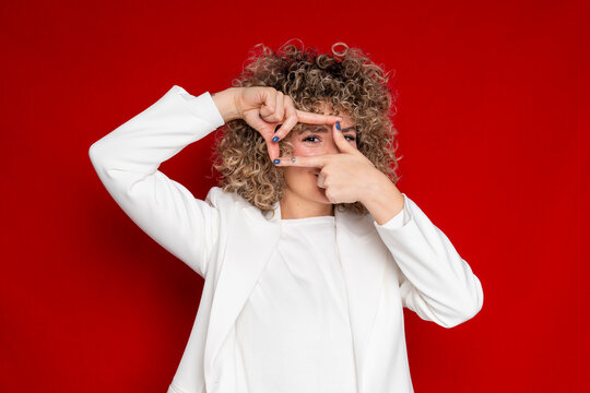 Fashionable woman in white blazer framing with hands against red background