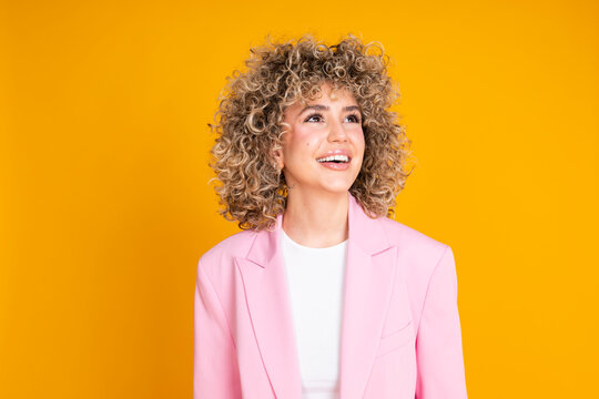 Businesswoman with curly hair in a pink blazer against a yellow background