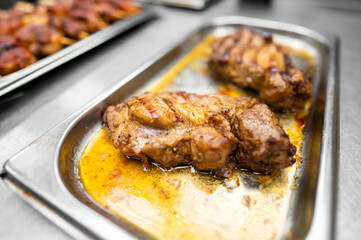 Succulent roasted meat sits in a metallic tray, glistening with juices. The savory dish exudes rich flavors, showcasing culinary expertise in a professional kitchen environment.
