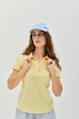 Young woman in soft yellow shirt and blue cap posing against a light background with elegance