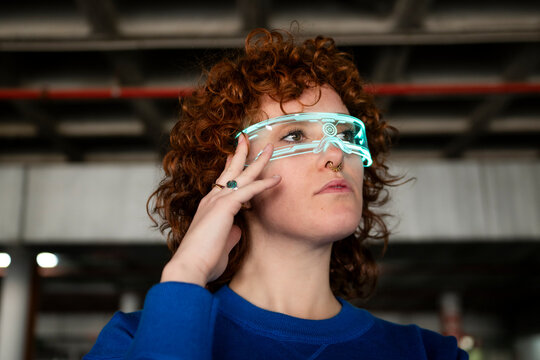 Young woman with curly hair wearing futuristic AR glasses indoors