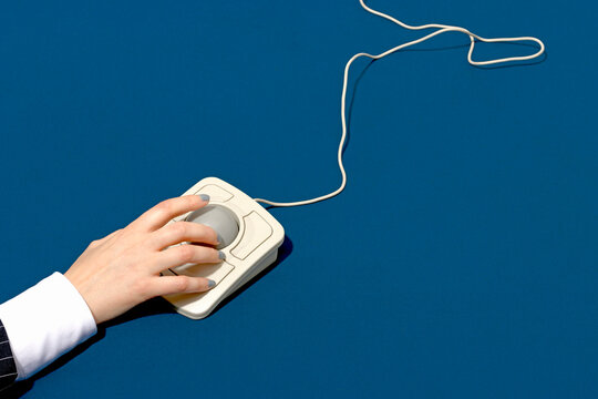 Hand using a vintage trackball mouse on a blue background