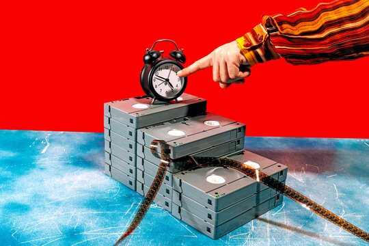 Hand pointing at alarm clock on stacked VHS tapes with red background
