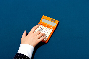 Closeup of a hand using a retro orange calculator on a blue background