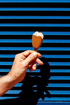Hand holding chocolate ice cream against a striped blue background outdoors