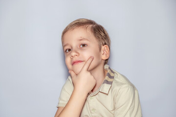 Young child with blond hair, wearing a light shirt with striped collar, rests chin on hand and gazes thoughtfully, striking a pose that conveys contemplation and curiosity