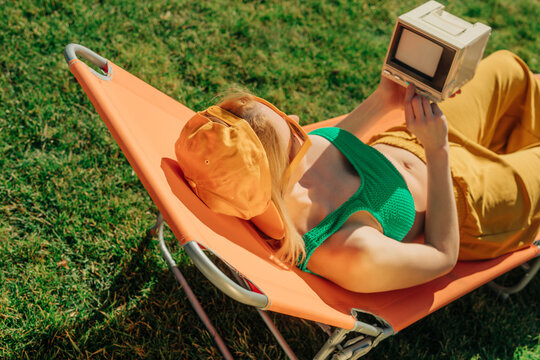 Woman relaxing on a sun lounger in the backyard watching a retro TV