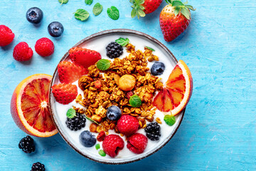Granola with yogurt and fresh fruit. Organic gourmet muesli, overhead flat lay shot on a blue background, with a copy space