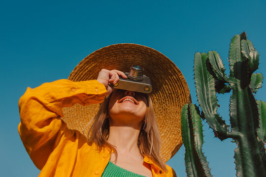 Stylish woman on vacation photographing with a vintage camera near a cactus
