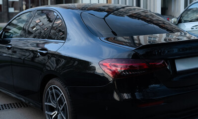 Black sedan parked in an urban area reflecting buildings in the late afternoon