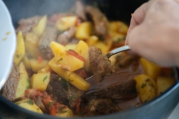 Cooking a hearty beef and potato stew in a pot with fresh vegetables and herbs on a cozy kitchen stove