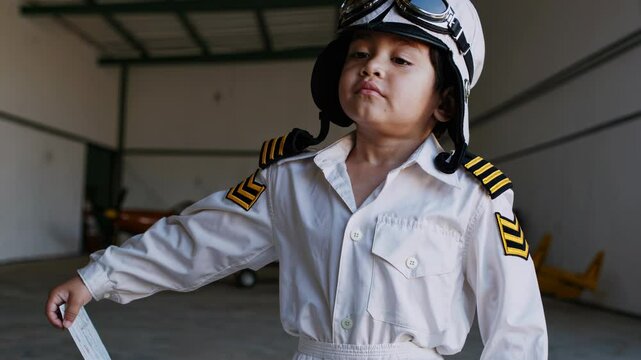 Adorable child wearing aviator costume standing in aircraft hangar, checking preflight checklist while embodying childhood dreams of aviation and future aspirations