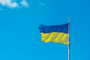 The Ukrainian flag fluttering in the wind against a light blue sky.