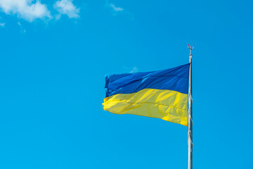 The Ukrainian flag fluttering in the wind against a light blue sky.