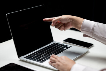 Businesswoman using laptop while touching or pointing at the laptop screen. Cellphone and tablet on the table. Mockup and copy space. Business and technology concept