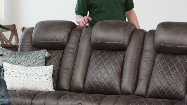 Workwear clad man halts behind leather sofa, plants hands in confident stance