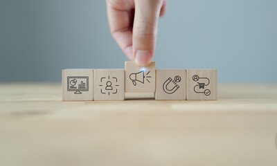 Marketing strategy planning with wooden blocks. A hand arranging wooden blocks with  icons representing data analytics, customer targeting, advertising, lead generation and sales process.