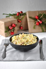 Traditional Russian salad olivier in a deep black plate. There are Christmas gift boxes nearby.