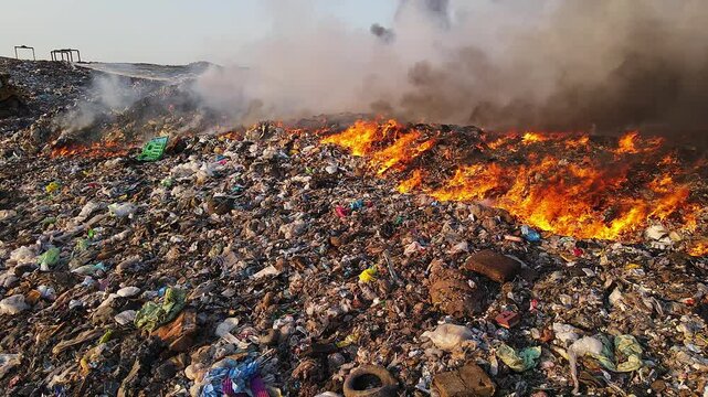 Flames raging across trash mound at landfill site in panning video