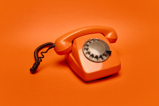 Bright orange rotary phone on bold orange background captures essence of retro design and analog communication, perfect for vintage ads, nostalgic posters, minimalist campaigns.