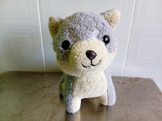 Adorable and fluffy plush dog toy with gray and cream fur, standing on a metallic surface against a tiled wall background.