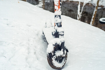 Public electric scooter covered with snow in the forest. Forgotten scooter in a winter park.