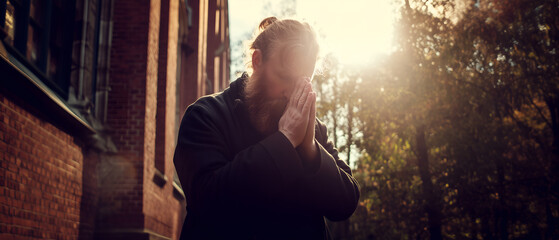 young bearded danish man praying outside in front of church; concept of bededag, denmark religious holiday celebration, may 16th; panoramic banner with copy space