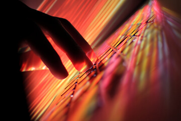 Silhouette of hand interacting with illuminated keyboard, red and orange light streaks create dynamic background, suggesting digital activity or technological interaction