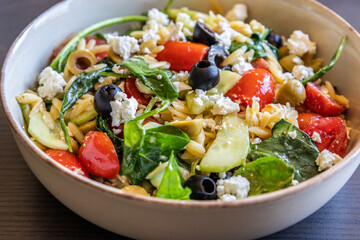  healthy orzo salad served in a bowl, made with fresh vegetables, black olives, and crumbled feta...