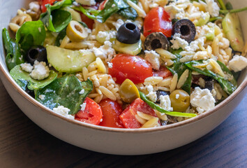  healthy orzo salad served in a bowl, made with fresh vegetables, black olives, and crumbled feta cheese close up