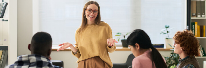 Group of diverse students engaging in studying foreign languages in bright classroom setting. Teacher standing and explaining with smiling face, surrounded by attentive students