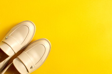 Beige shoes stand on a yellow background with space for text.