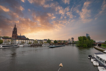 Obraz premium Serene view of the Main River in Frankfurt, Germany, featuring the Gothic style Frankfurt Cathedral, modern high rises, and a barge on the water.
