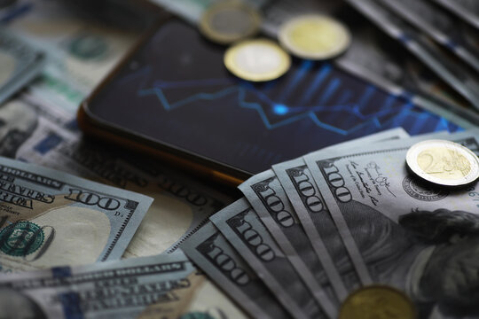 Smartphone Displaying Stock Market Trends Surrounded by US Dollar Banknotes and Coins - Powered by Adobe