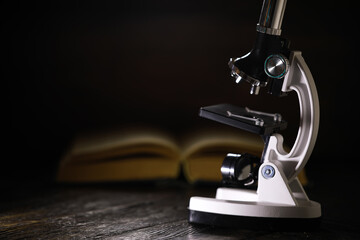 Vintage Microscope on Dark Wooden Table with Open Book in Background